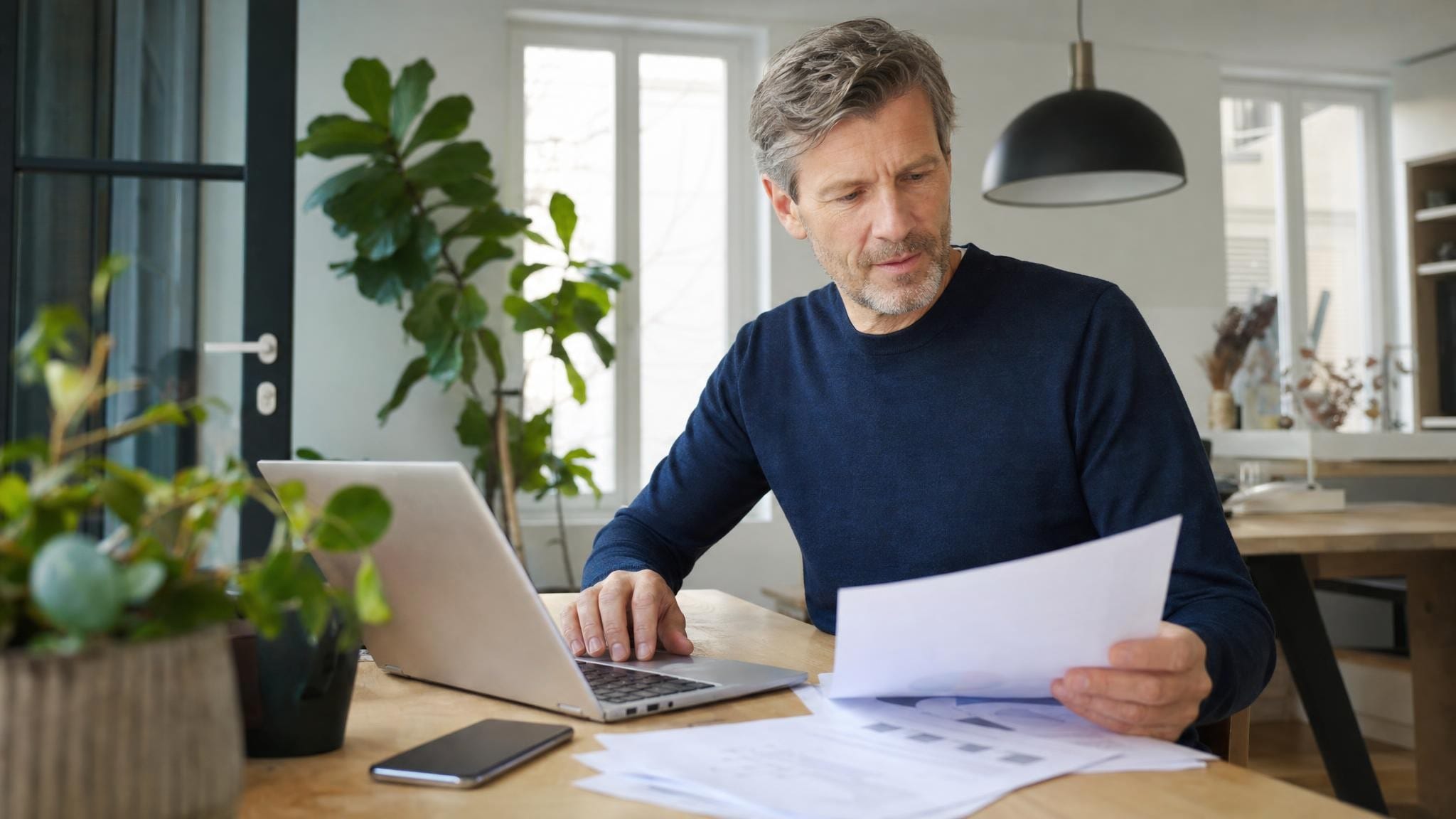 Man werkt aan een laptop met documenten op tafel, bezig met zijn taken als gevolmachtigde