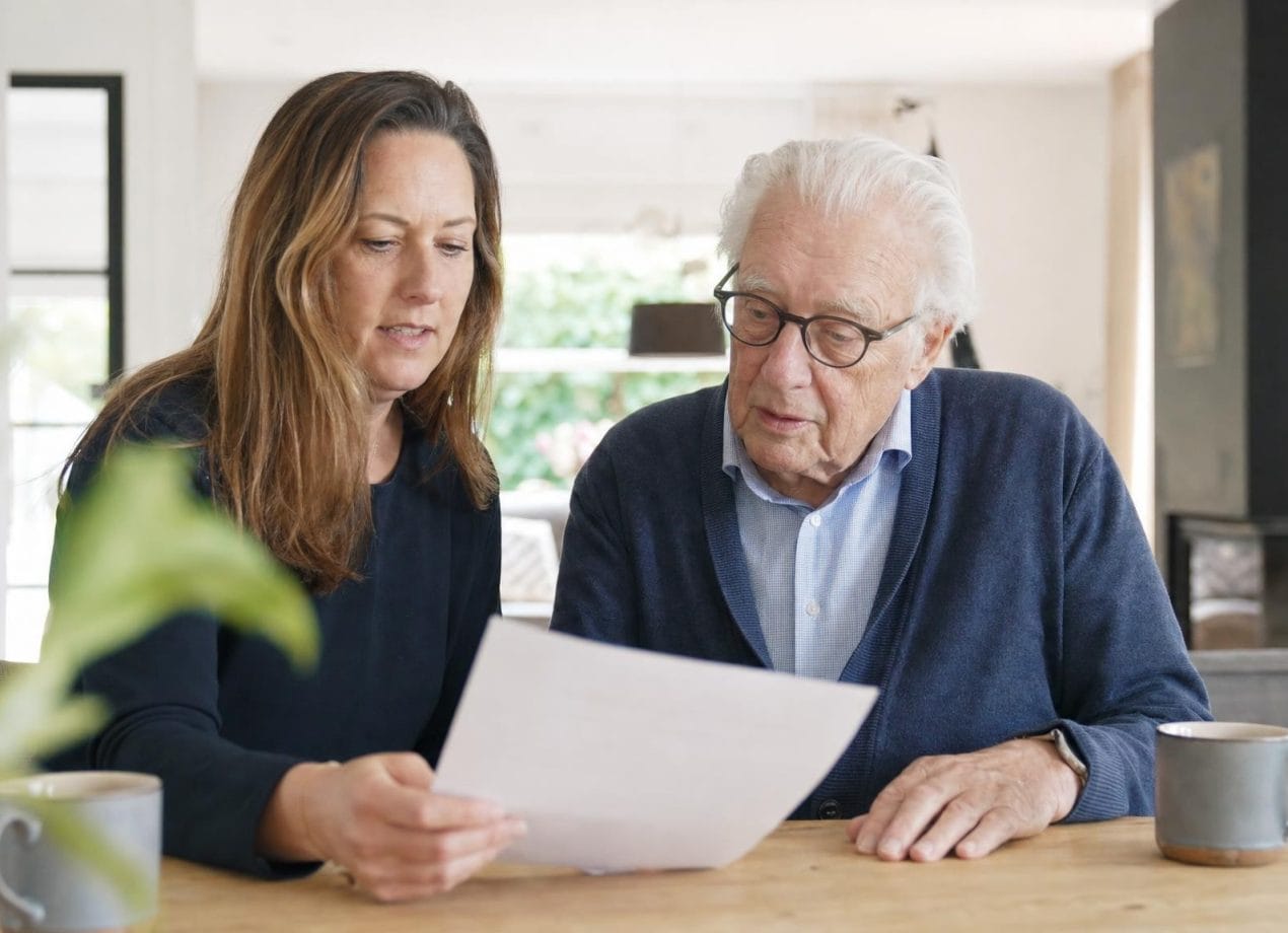 Oudere vader bespreekt samen met zijn volwassen dochter aan tafel een document over een behandelverbod, in een licht modern interieur