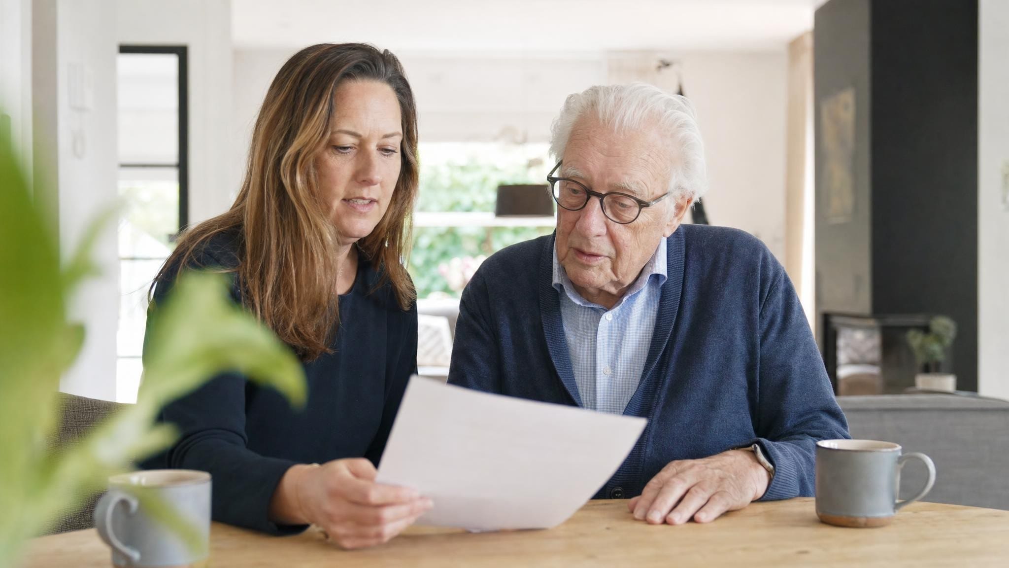 Oudere vader bespreekt samen met zijn volwassen dochter aan tafel een document over een behandelverbod, in een licht modern interieur